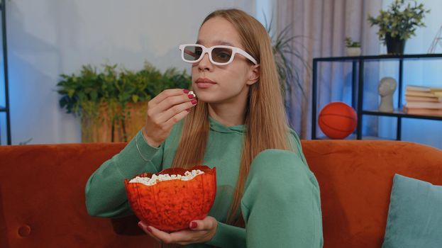 Excited teen girl sitting on sofa eating popcorn and watching interesting tv serial, sport game, film, online social media movie content online at home. Young child kid enjoying domestic entertainment