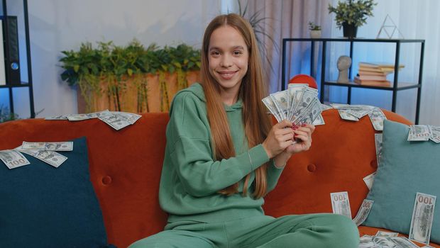 Successful happy rich business woman girl counting money cheering up with high profits, lottery game win, satisfied of wealth income earnings salary, on home room couch full of dollar cash banknotes
