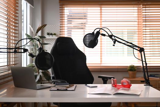 Home studio podcast interior with professional microphone, laptop and wireless headphone. Technology and audio equipment concept.