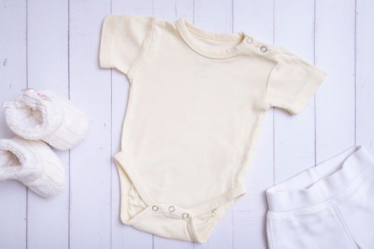 Yellow baby bodysuit mockup for logo, text or design on wooden background top view