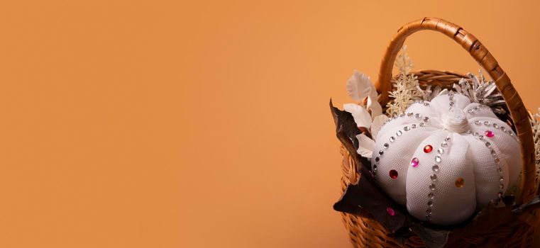 Banner with white decorative hand made pumpkin with shiny stones and fall leaves in basket on colored background. Autumn harvest concept.