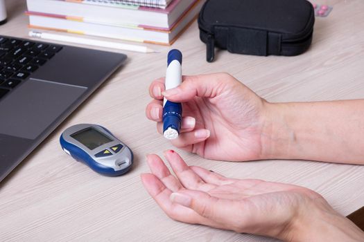 Female hands with a glucometer at the desk. The lifestyle of a person with diabetes, measuring the level of glucose in the blood.