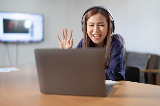 cheerful asian girl have online video call broadcast meet bloggers say hi wave hand sit table use laptop in house indoors.