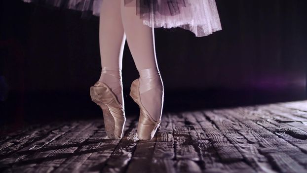 close up, in rays of spotlight, on stage of old theater hall. ballerina in white ballet skirt, raises on toes in pointe shoes, performs elegantly a certain ballet exercise, en tournaht suivi. High quality photo