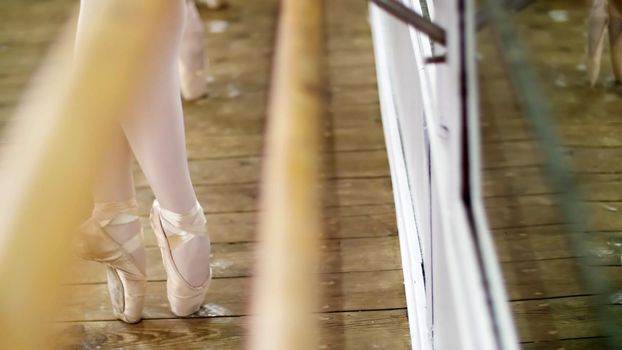 close up, in dancing hall, Young ballerinas in purple leotards perform pas de bourre suivi in the fifth position, standing on toes in pointe shoes near barre at mirror in ballet class... High quality photo