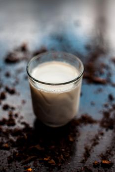 HIGH ANGLE SHOT OF GLASS OF MILK WITH SOME COCOA POWDER SPRINKLED ON BLACK GLOSSY SURFACE.