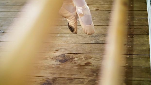 close up, in dancing hall, ballerina performs pas soute, jumping in ballet shoes near barre, on an old wooden floor, in ballet class. High quality photo