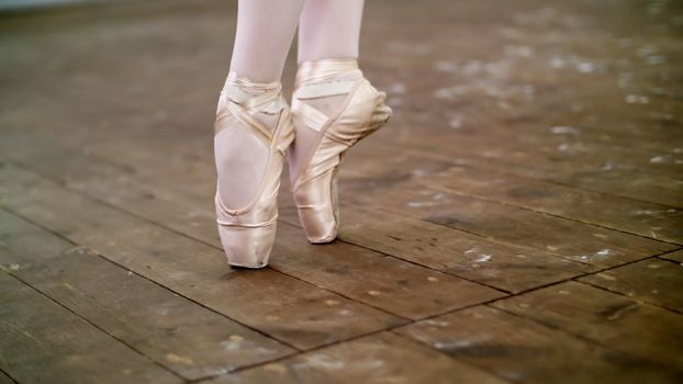 close up, in dancing hall, ballerina perform step pointe , She is standing on toes in pointe shoes elegantly , on an old wooden floor, in ballet class. High quality photo