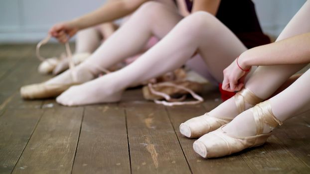 close up, ballerinas change their shoes into special ballet shoes, pointe shoes, lace with ballet ribbons, on an old wooden floor, in ballet class. High quality photo