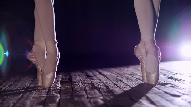 close up, in rays of spotlight, on the stage of the old theater hall. ballerinas standing on toes in pointe shoes, performs elegantly a certain ballet exercise, pas de bourre suivi. High quality photo