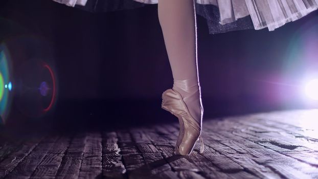 close up, in rays of spotlight, on stage of old theater hall. ballerina in white ballet skirt, rotates on toe in pointe shoe, performs elegantly a certain ballet exercise, tour,pointe. High quality photo