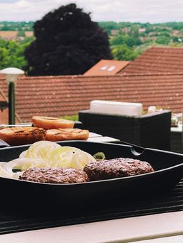 Cooking minced beef burger on cast iron grill skillet outdoors, red meat on frying pan, grilling food in the garden, English countryside living concept
