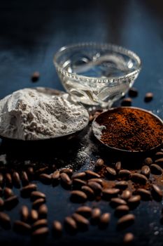 Coffee face mask for skin whitening on a black shiny wooden surface consisting of some coffee powder, lukewarm water, and rice flour.