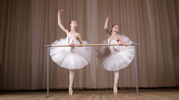 ballet rehearsal, in old theater hall. Young ballerinas in white ballet skirts, tutus, are engaged at ballet, perform elegantly a certain ballet exercise, pass , attidude, standing near barre. High quality photo