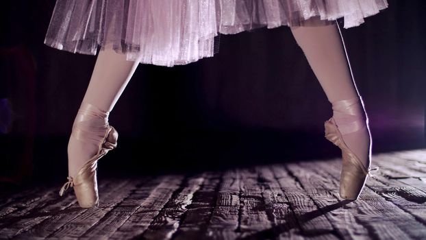 close up, in rays of spotlight, on the stage of the old theater hall. ballerina in white ballet skirt, raises on toes in pointe shoes, performs elegantly a certain ballet exercise, relleve. High quality photo