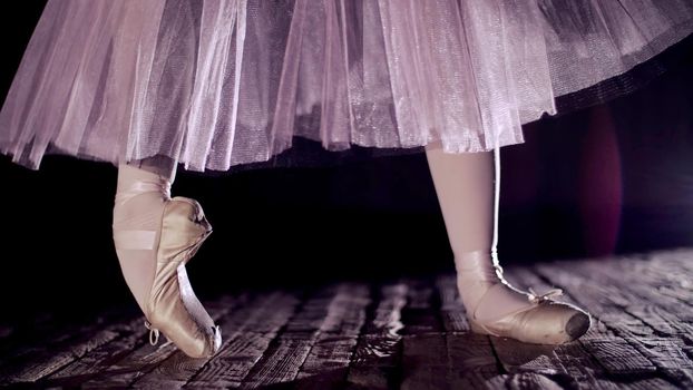close up, in rays of spotlight, on stage of old theater hall. ballerina in white ballet skirt, raises on toes in pointe shoes, performs elegantly a certain ballet exercise, pointe ,tendu. High quality photo