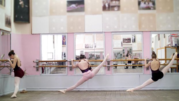 in dancing hall, Young ballerinas in black leotards stretching at barre, on pointe shoes, elegantly, standing near barre at mirror in ballet class. High quality photo