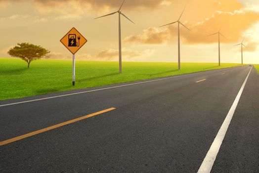 Road in green field and Electric car road sign charging station with wind turbines backgrounds.