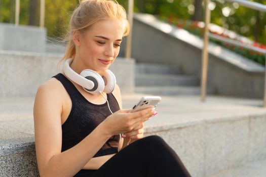 Sport and Fitness Young Adult Caucasian Woman Using Smartphone Concrete Floor Resting after morning Workout Outdoor Summer Park Athletic Female Take a Break Use mobile Phone