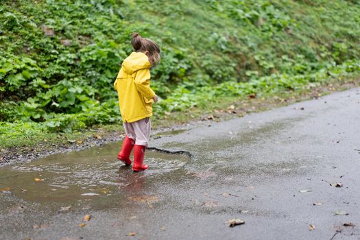 Playful girl wearing yellow raincoat while jumping in puddle during rainfall Happy childhood