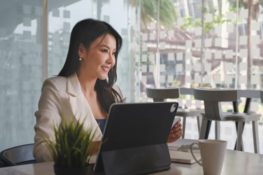 Asian Business woman sitting in office with laptop computer on wooden desk.