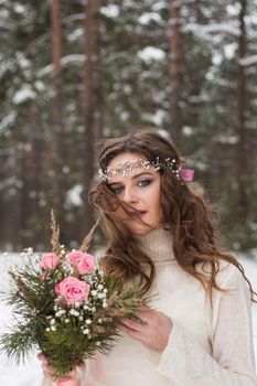 Beautiful bride in a white dress with a bouquet in a snow-covered winter forest. Portrait of the bride in nature.