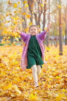 Joyful laughing caucasian girl 5 y.o. having fun in autumn park runs under the leaf fall and rejoices in autumn.