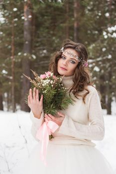 Beautiful bride in a white dress with a bouquet in a snow-covered winter forest. Portrait of the bride in nature.