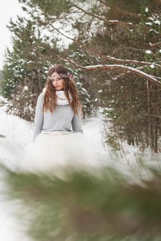 Beautiful bride in a white dress with a bouquet in a snow-covered winter forest. Portrait of the bride in nature.