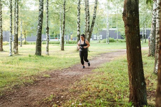 A charming brunette woman plus-size body positive practices sports in nature.