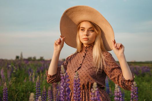 A beautiful woman in a straw hat walks in a field with purple flowers. A walk in nature in the lupin field.