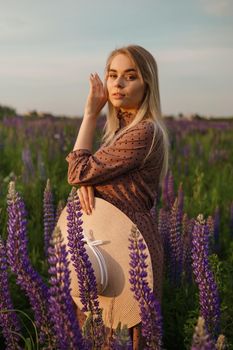 A beautiful woman in a straw hat walks in a field with purple flowers. A walk in nature in the lupin field.