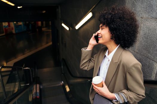 latin business woman talking happy by phone on the escalator of the subway station, concept of urban lifestyle and public transport, copy space for text