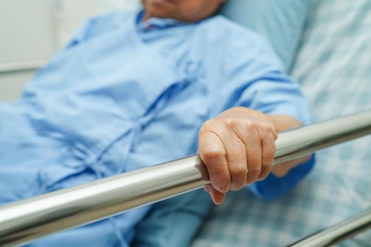Asian elder senior woman patient holding bed rail while lie down with hope waiting her family in hospital.