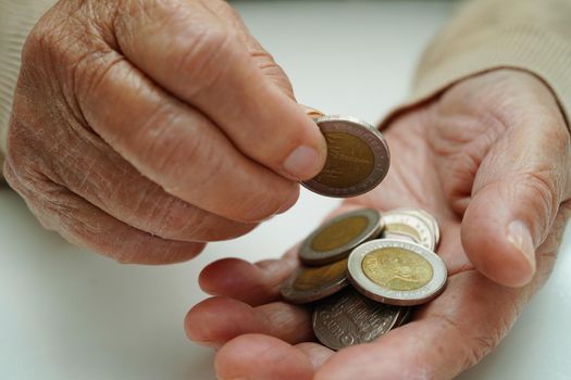 Retired elderly woman counting coins money and worry about monthly expenses and treatment fee payment.