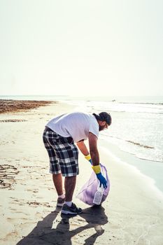 man collecting plastics that pollute the sea in plastic bag, people helping to keep nature clean and picking up the waste from beach, volunteer campaign to cleaning on the beach, vertical photo