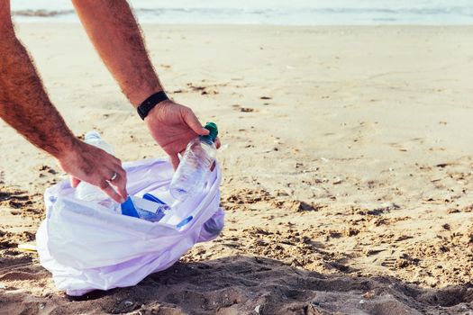 hands of an activist picking up plastics and trash that pollutes the sea on a bag on a sunny day, cleaning on the beach, campaign to clean volunteer concept, copy space for text