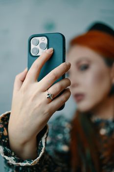 Attractive woman posing takes selfie on iPhone 13 pro. Gadget with triple-lens camera. Focus on foreground. Close-up of female's hand holding smartphone in case. Bishkek, Kyrgyzstan - January 24, 2022