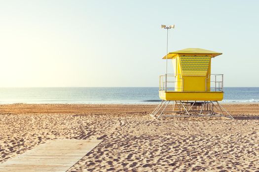 summer scene with a colorful yellow lifeguard house on the beach, at sunset with clean sky in the background, copy space for text