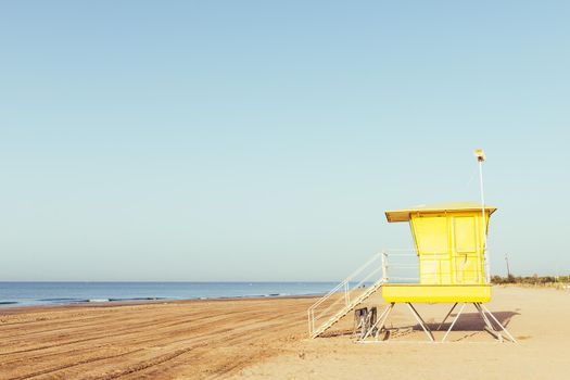 summer scene with a colorful yellow lifeguard tower on the beach, at sunset with clean sky in the background, copy space for text