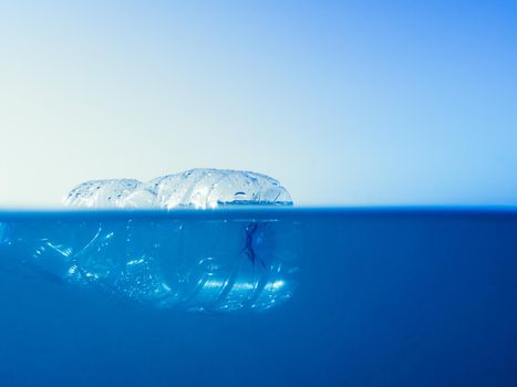plastic waste at the ocean, photo half surface half underwater of a plastic bottle floating in the sea at the water surface, environmental problem with plastics pollution, copy space for text