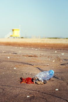 vertical photo of a plastic bottle and garbage lies on the sand of the beach polluting the sea and the marine life, concept of pollution control of the oceans by plastic