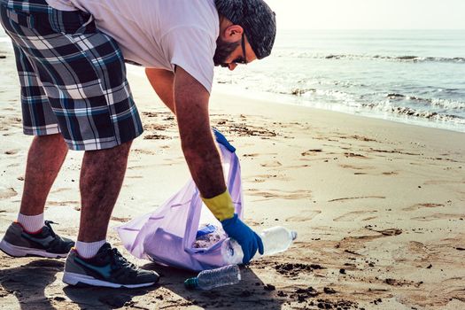 man collecting plastics washed up by the sea in plastic bag, people helping to keep nature clean and picking up the waste from shore, volunteer campaign to cleaning on the beach