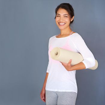 Start today. a sporty young woman holding her yoga mat against a grey background