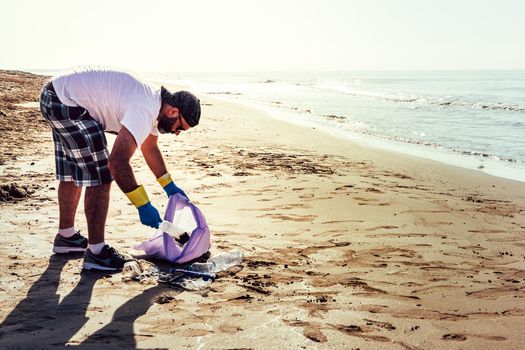 man collecting waste washed up by the sea in plastic bag, people helping to keep nature clean and picking up the garbage from shore, volunteer campaign to cleaning on the beach