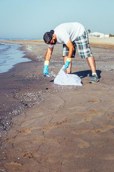 man collecting waste that pollute the ocean in plastic bag, people helping to keep nature clean and picking up the plastics from sea, volunteer campaign to cleaning on the beach, vertical photo