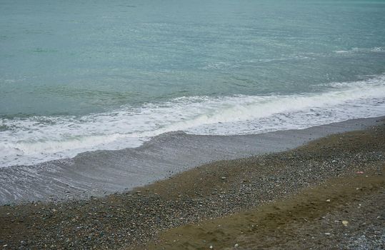 Sea shore with pebbles, wet sea pebbles on the beach and quiet sea surf. Restless sea and waves