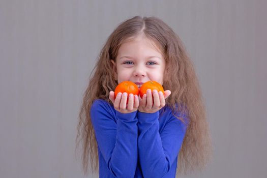 Happy and smiling child kid showing mandarins in hands on brown background looking at camera portrait of caucasian little girl of 5 years in blue