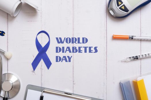 World Diabetes Day text with glucometer, stethoskope and syringes with a tablet on a wooden background, top view.
