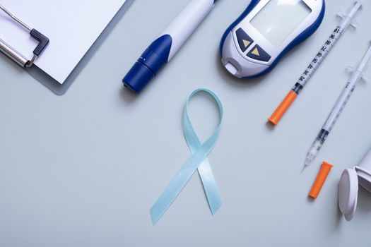 Blue ribbon and glucometer, medical supplies on color background top view with copy space. World diabetes day concept.